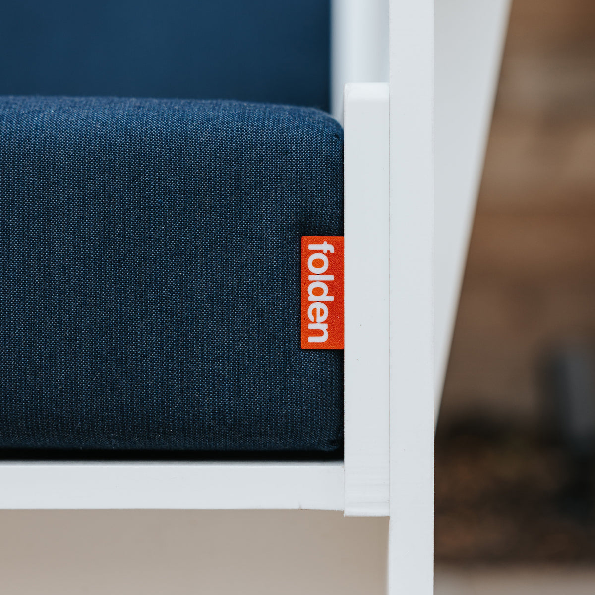 Close-up of a dark blue FOLDEN Club Chair cushion with an orange brand label beside the white frame.