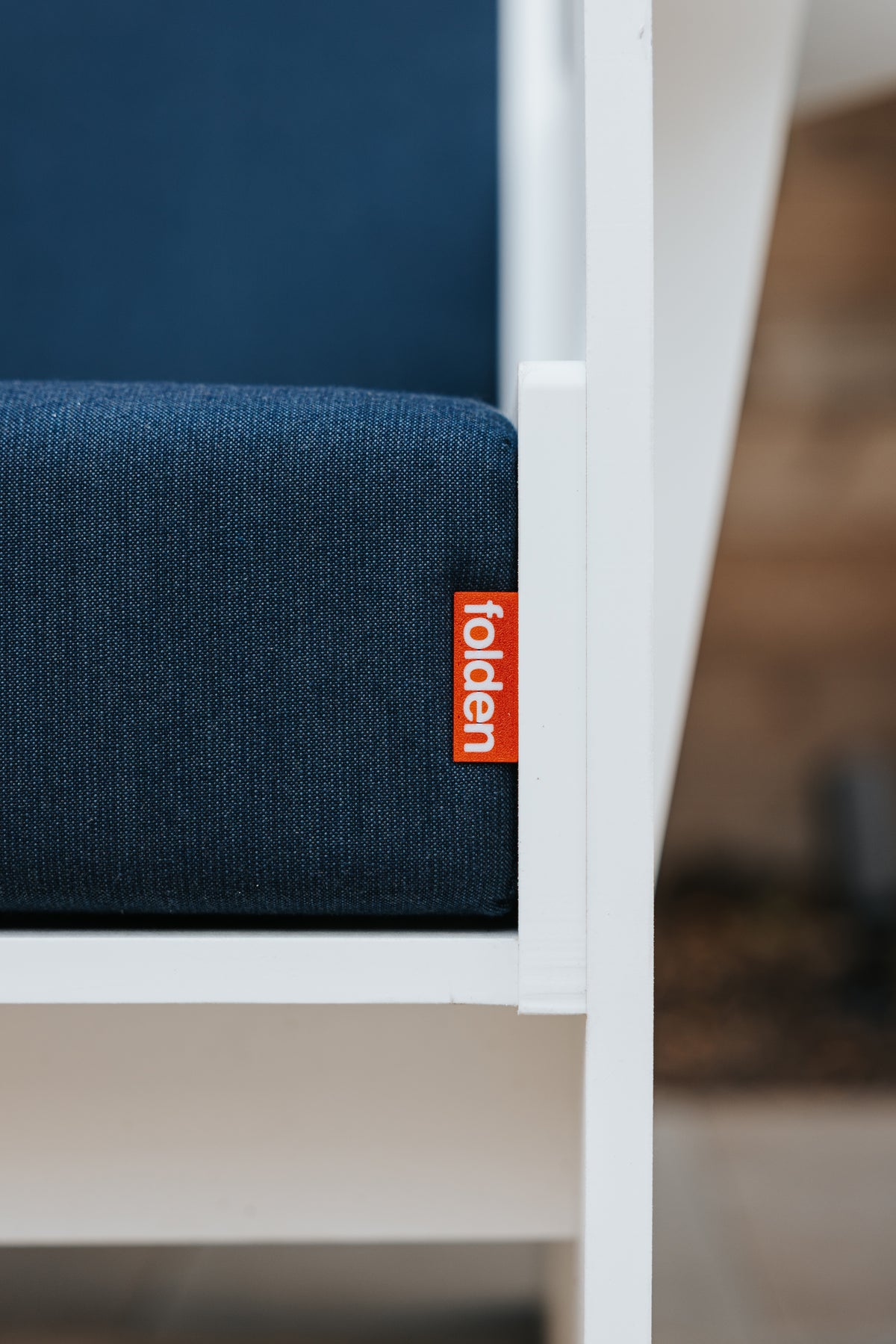 Close-up of a dark blue FOLDEN Club Chair cushion with an orange brand label beside the white frame.