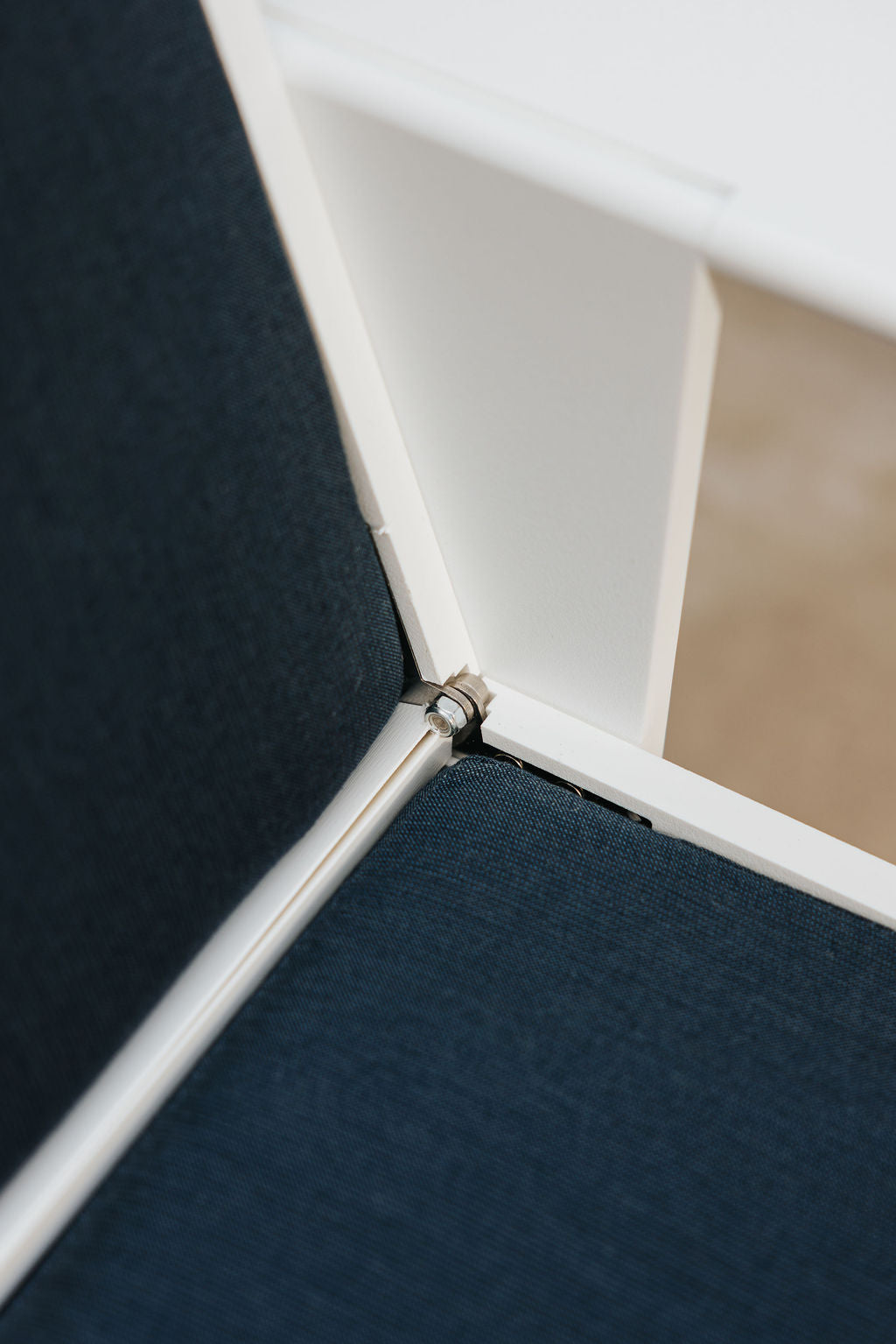 Close-up of the metal hinge joining the white FOLDEN Club Chair frame beside its dark blue cushions.