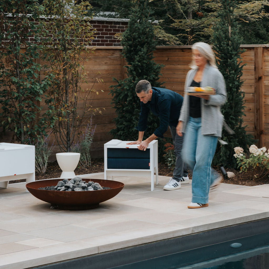 Man closing a white FOLDEN Club Chair around its dark blue cushions on a poolside patio.