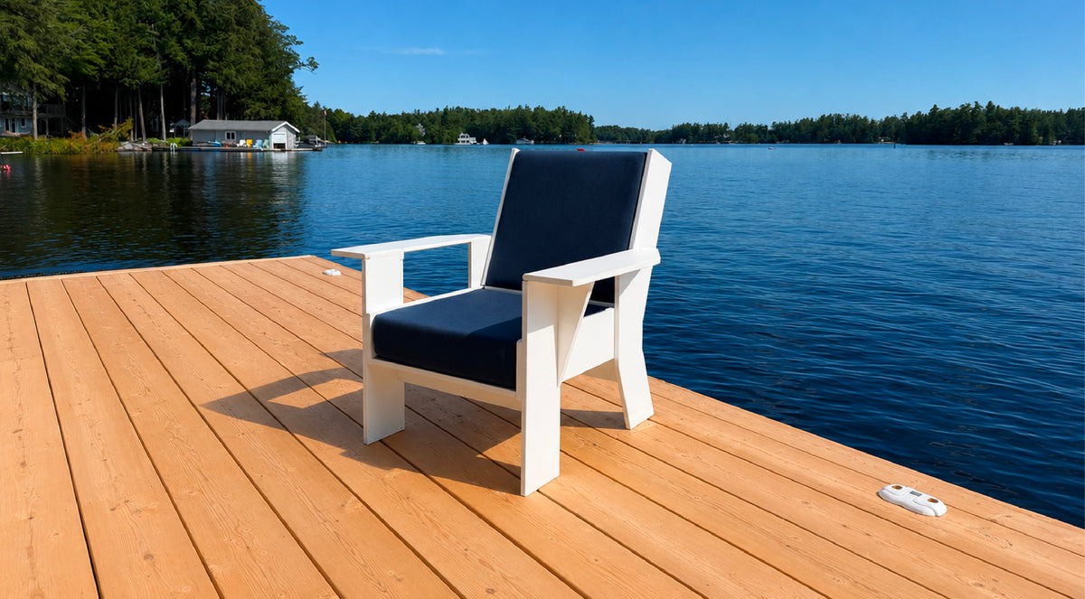 White FOLDEN Club Chair open for seating, with dark blue cushions on a sunny lakeside dock.